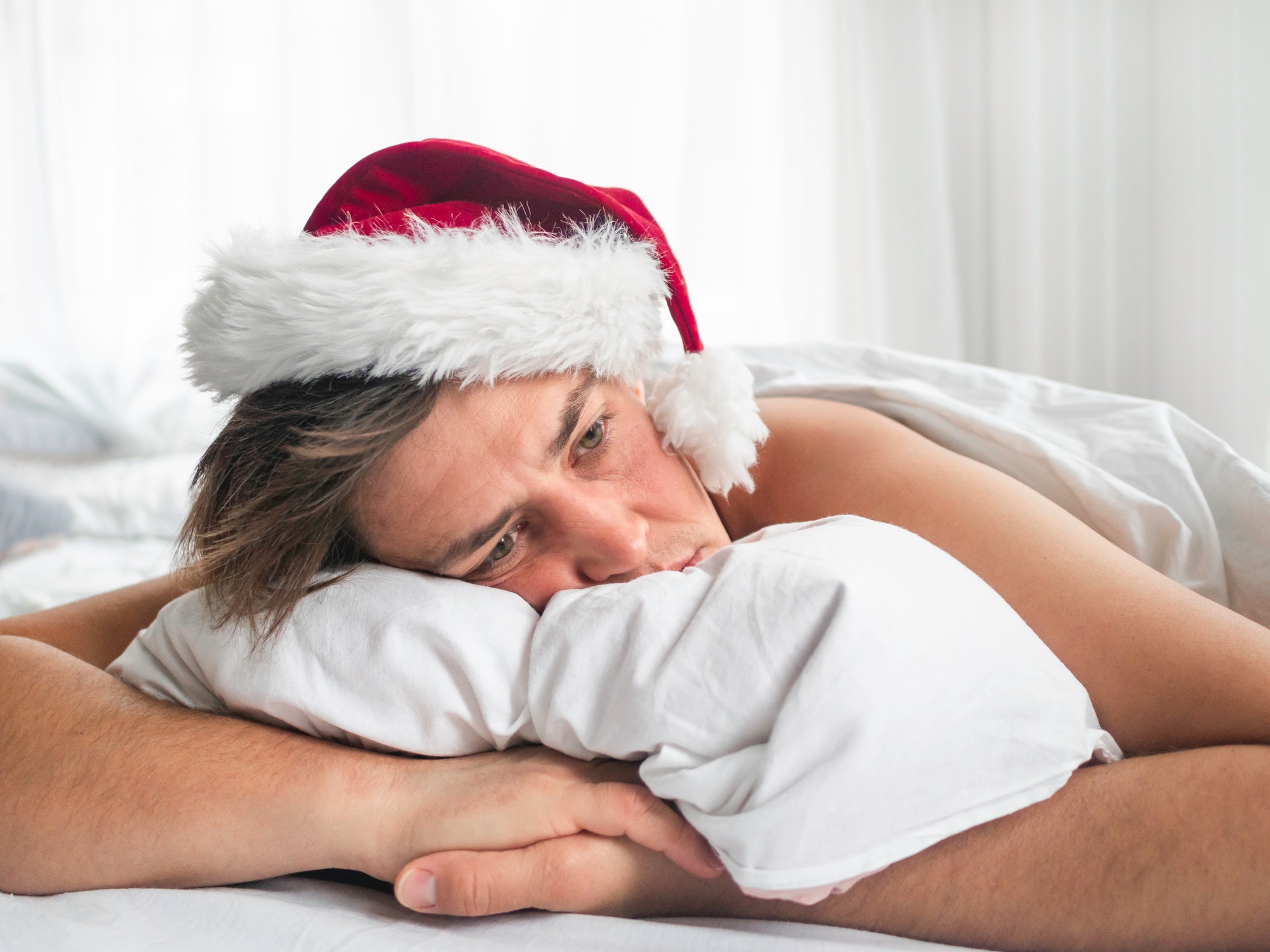 Man in Santa hat is waking up after Christmas. He is suffering of headache after New Year party.